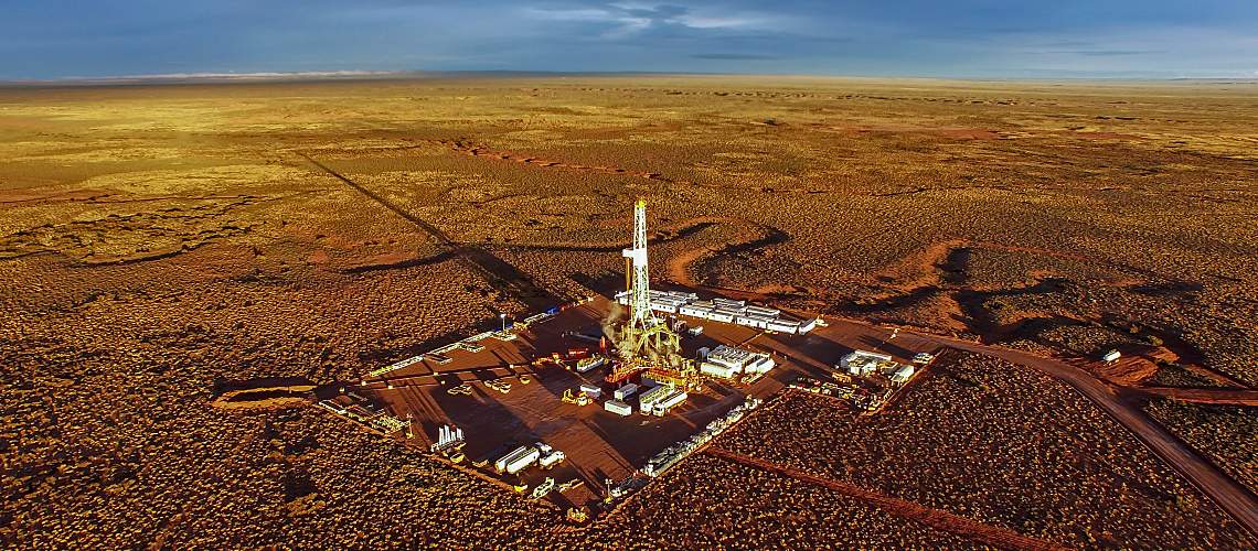 Hydraulic fracturing equipment at sunset in a parched landscape.