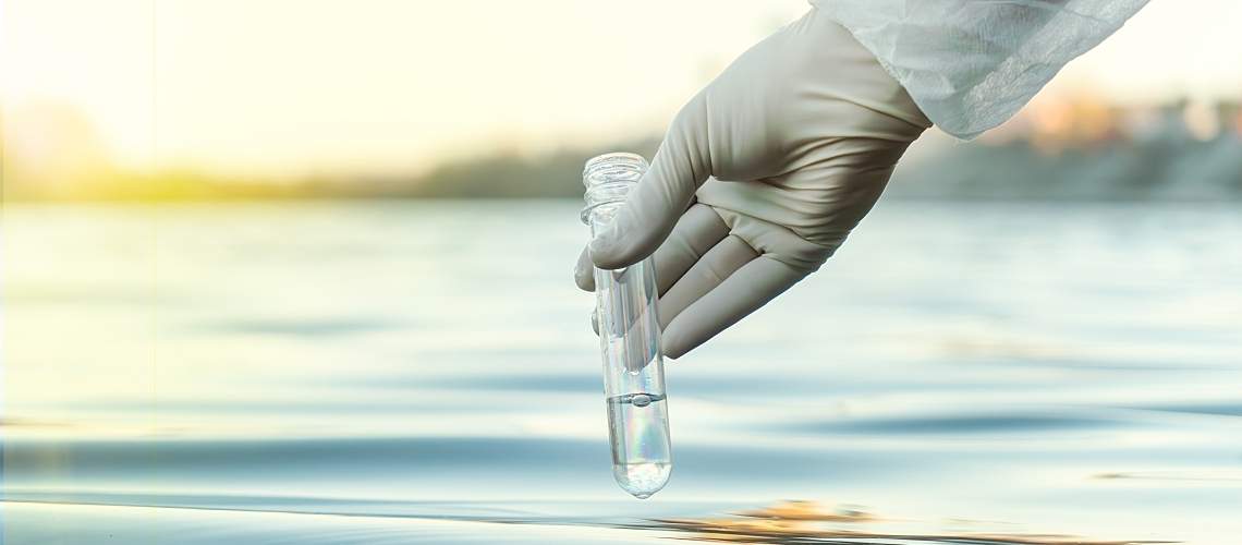 A gloved hand fills a test tube with water.