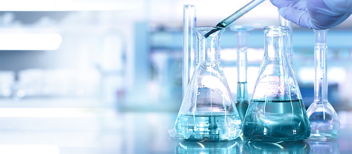 Hand of scientist using a dropper to insert blue liquid into a flask.