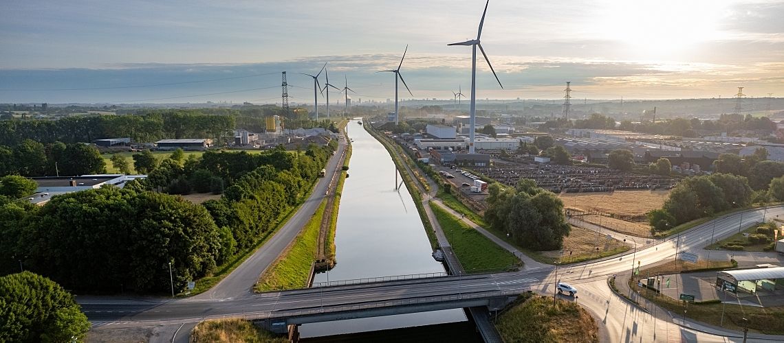 Aerial image of a modern landscape at dawn with waterway transportation and wind turbines.