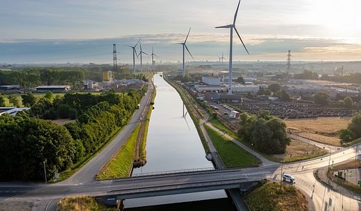 Aerial image of a modern landscape at dawn with waterway transportation and wind turbines.