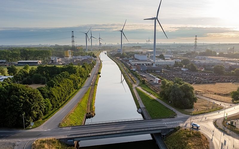 Aerial image of a modern landscape at dawn with waterway transportation and wind turbines.