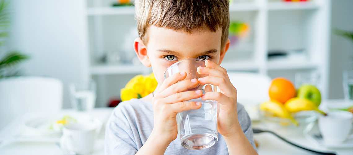 Young child drinks cold well water from a glass in the kitchen.