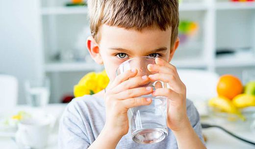 Young child drinks cold well water from a glass in the kitchen.