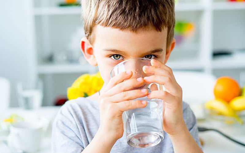 Young child drinks cold well water from a glass in the kitchen.