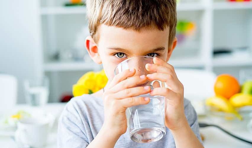 Young child drinks cold well water from a glass in the kitchen.