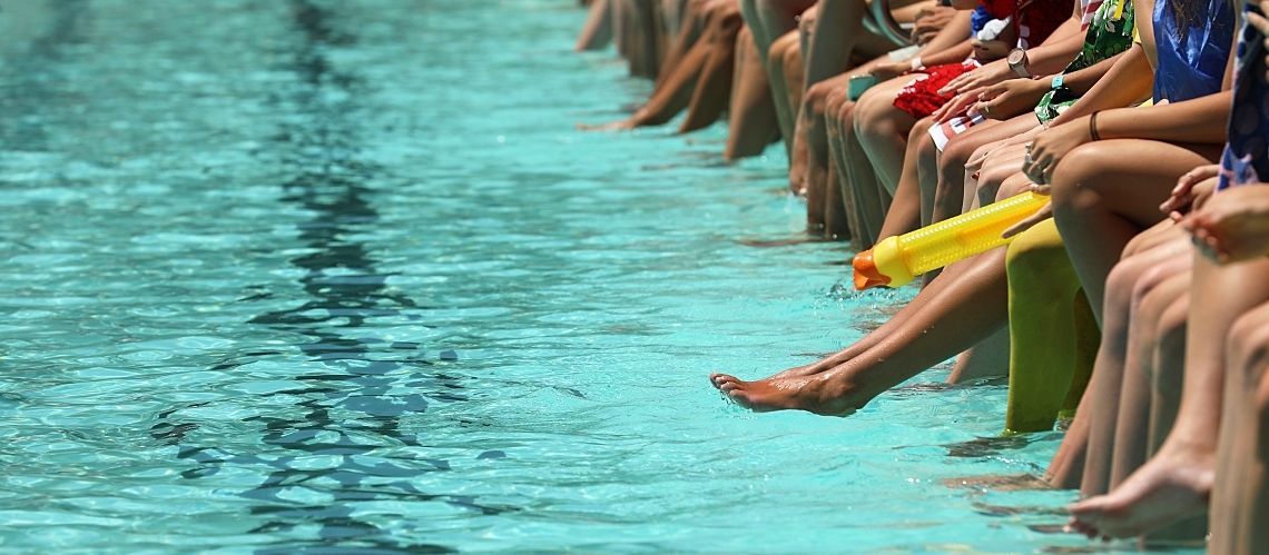 A bright aqua blue swimming pool with people sitting, dangling their feet and toes.