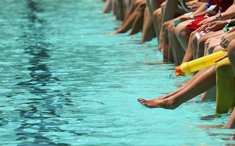 A bright aqua blue swimming pool with people sitting, dangling their feet and toes.
