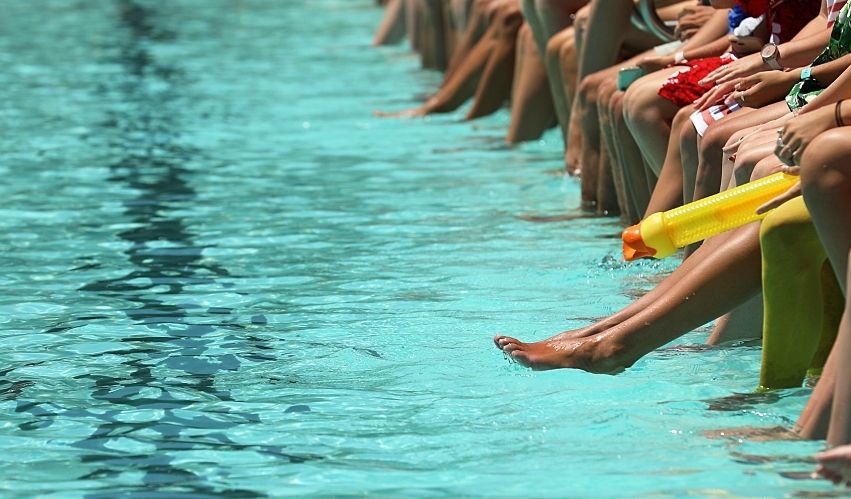 A bright aqua blue swimming pool with people sitting, dangling their feet and toes.
