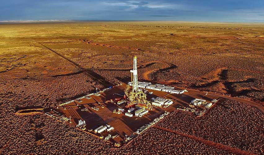 Hydraulic fracturing equipment at sunset in a parched landscape.