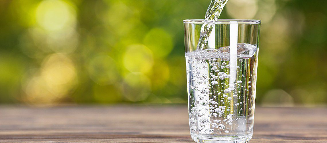 Water from a jug pouring into glass with natural green background.