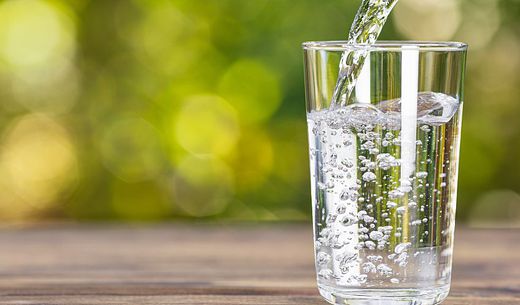 Water from a jug pouring into glass with natural green background.