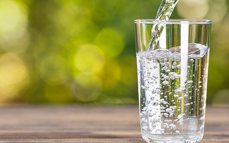 Water from a jug pouring into glass with natural green background.