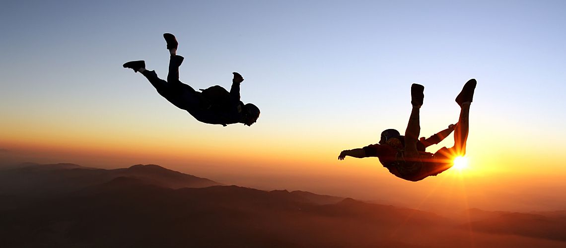 Two people skydiving during sunset.