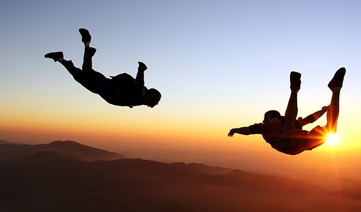 Two people skydiving during sunset.