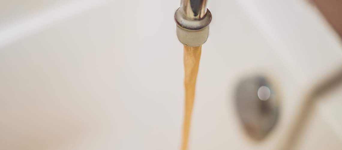 Dirty brown running water falling into a white sink.