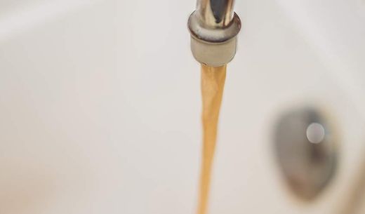 Dirty brown running water falling into a white sink.