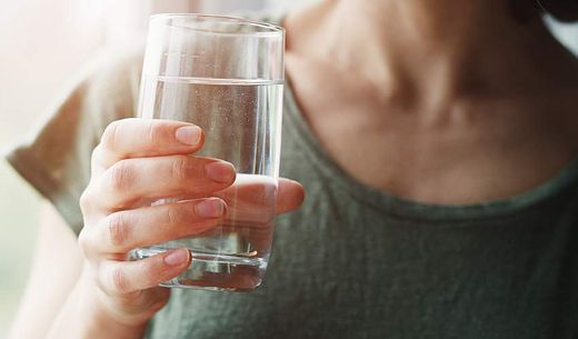 A young woman holds a glass of water.