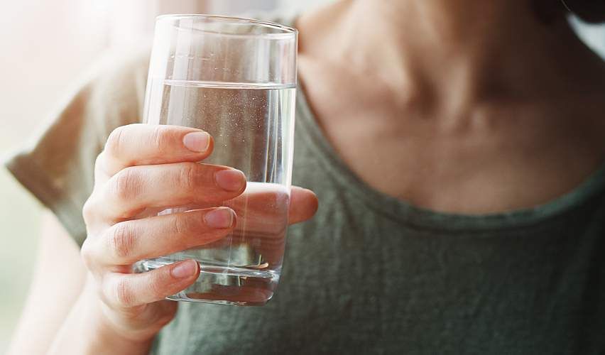 A young woman holds a glass of water.