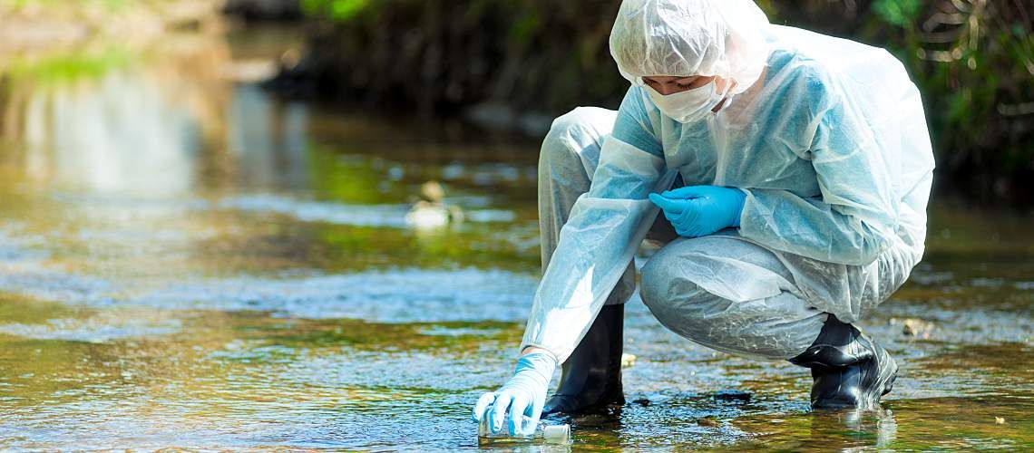 A researcher in a hazmat suit takes water for analysis.