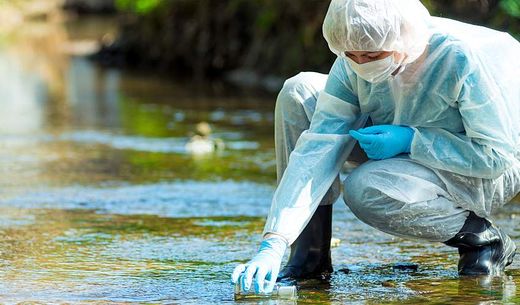 A researcher in a hazmat suit takes water for analysis.