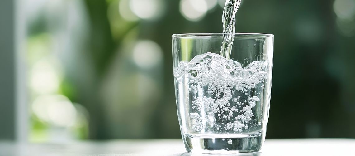 Water pours into a glass against a green blurred background.