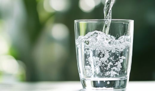 Water pours into a glass against a green blurred background.