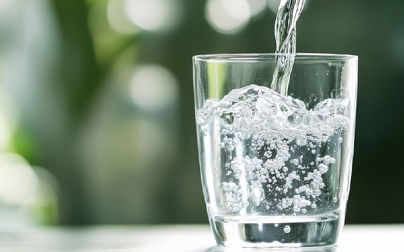 Water pours into a glass against a green blurred background.