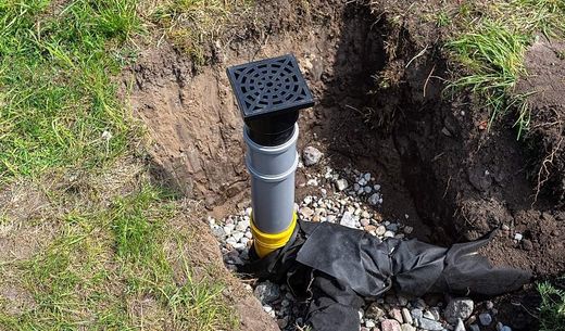 Overflow and infiltration well connected to drainage pipes, buried in a pit covered with stones.