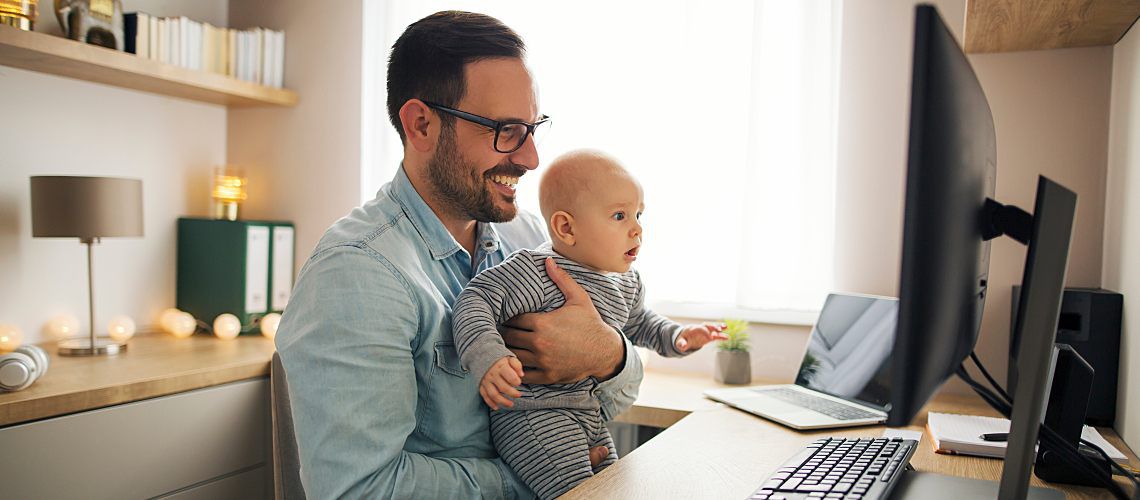 Dad on the computer while holding a baby.