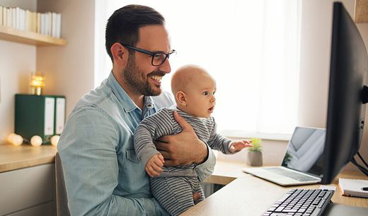 Dad on the computer while holding a baby.