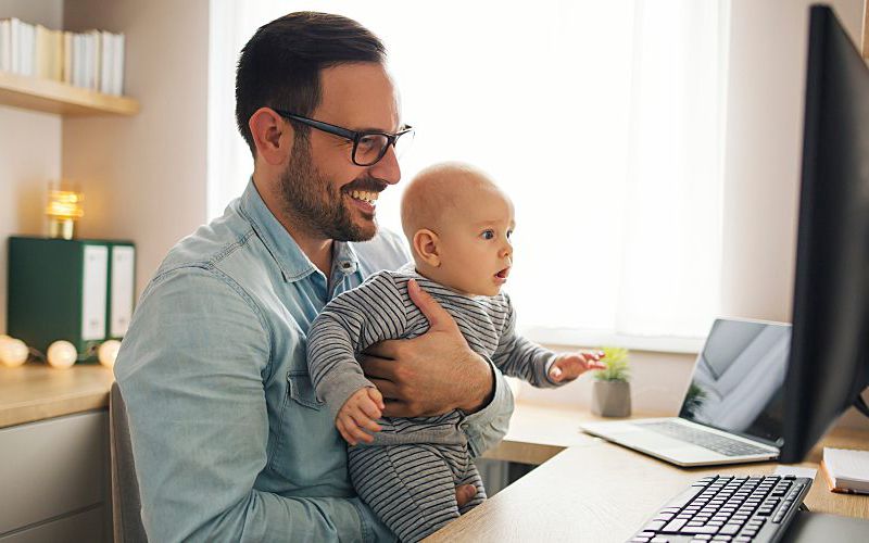 Dad on the computer while holding a baby.