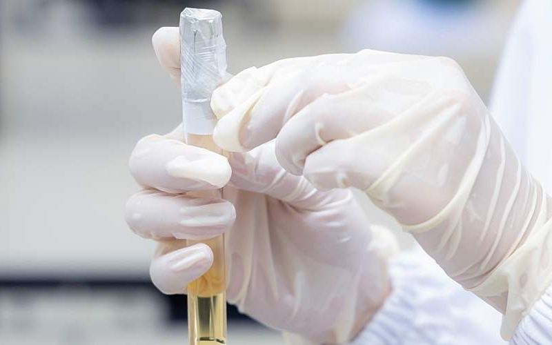 A gloved hand holding taped vial sample.