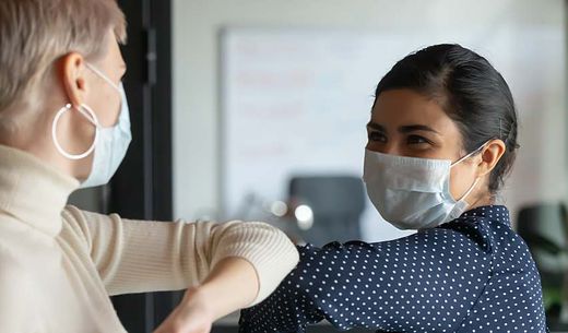 Two women interacting wearing face masks.