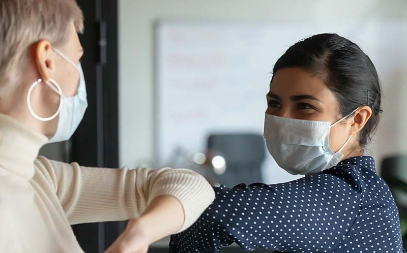 Two women interacting wearing face masks.