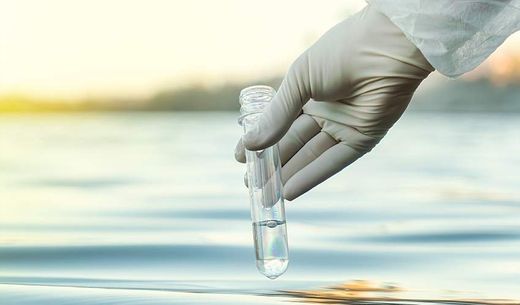 A gloved hand fills a test tube with water.
