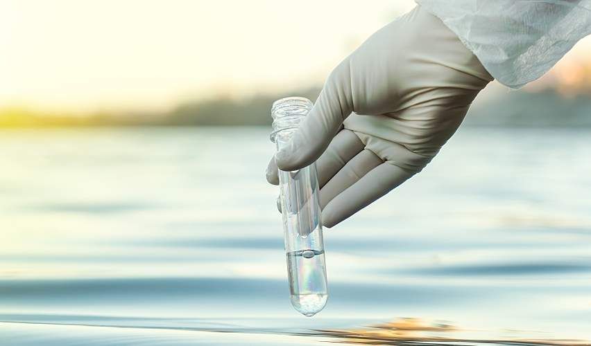 A gloved hand fills a test tube with water.