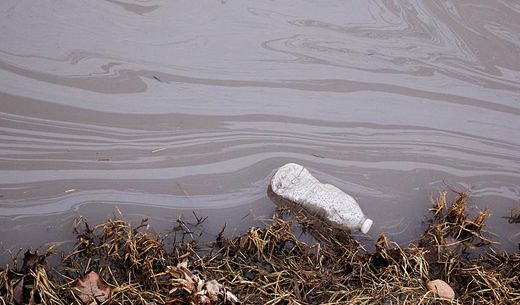 Floating water bottle in a polluted stream