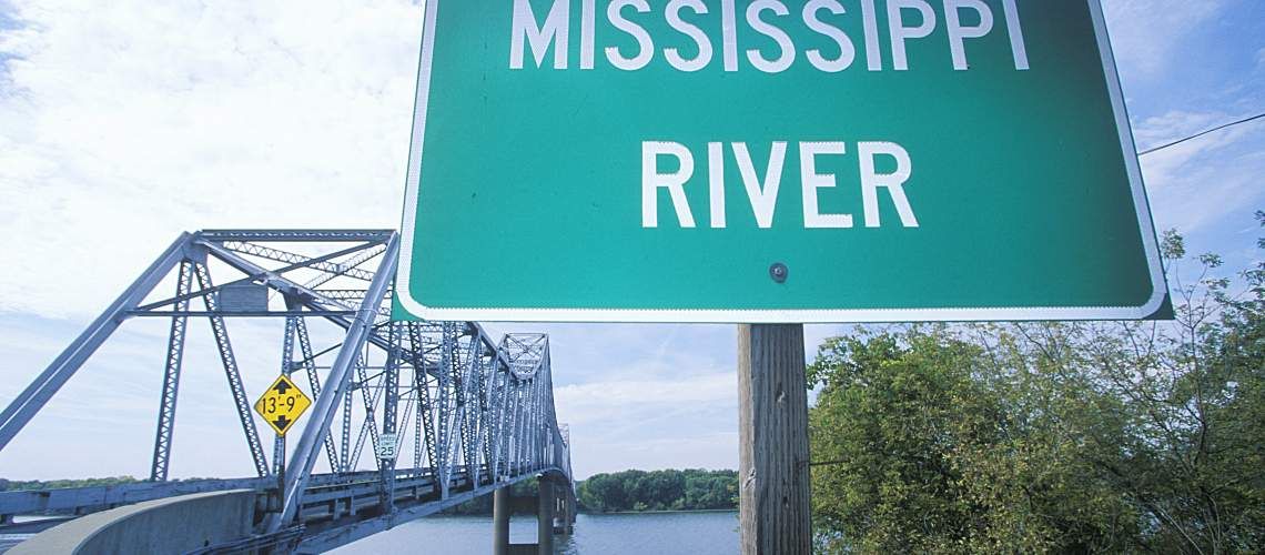 Mississippi River sign in front of a truss bridge over a stretch of river