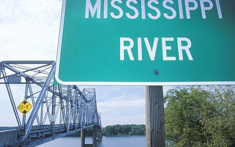 Mississippi River sign in front of a truss bridge over a stretch of river