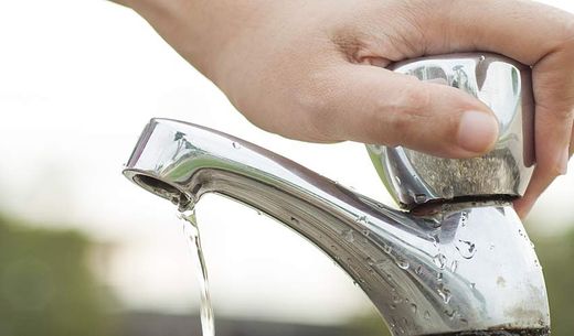 A hand turns off a faucet.