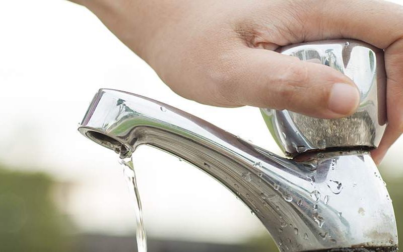 A hand turns off a faucet.