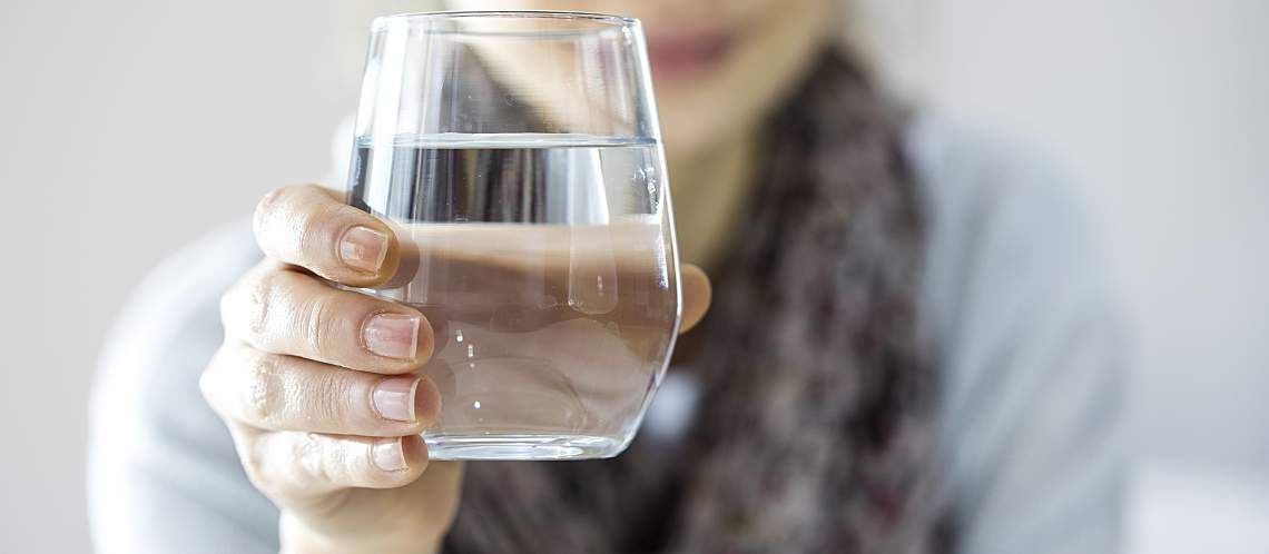 A young woman holds a glass of water.
