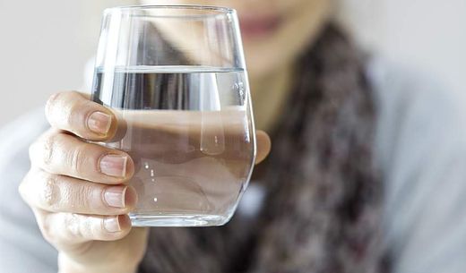 A young woman holds a glass of water.