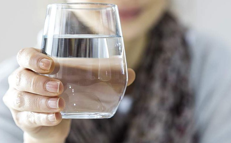 A young woman holds a glass of water.