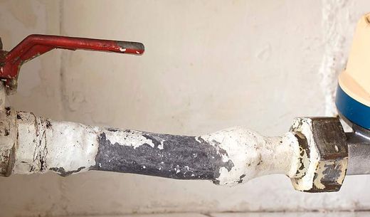 An old lead pipe with a red shut-off valve.