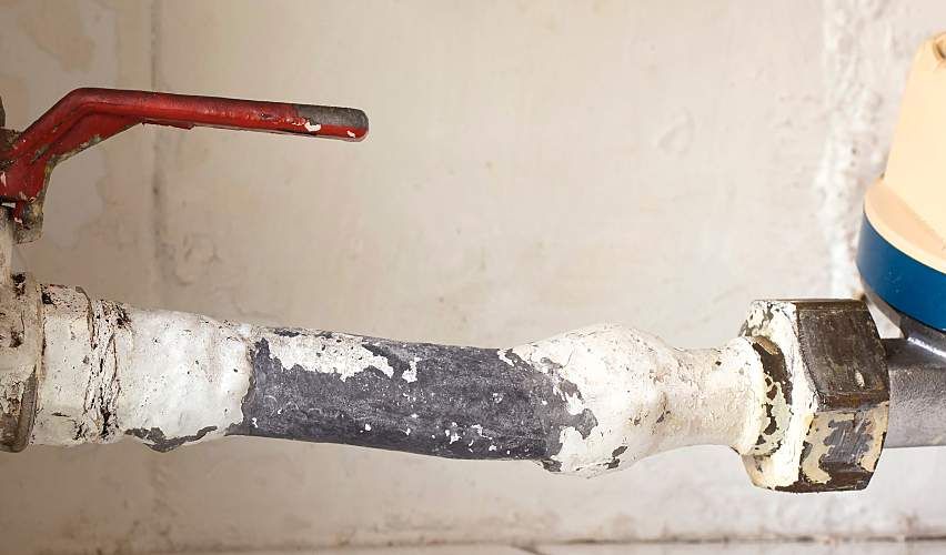 An old lead pipe with a red shut-off valve.