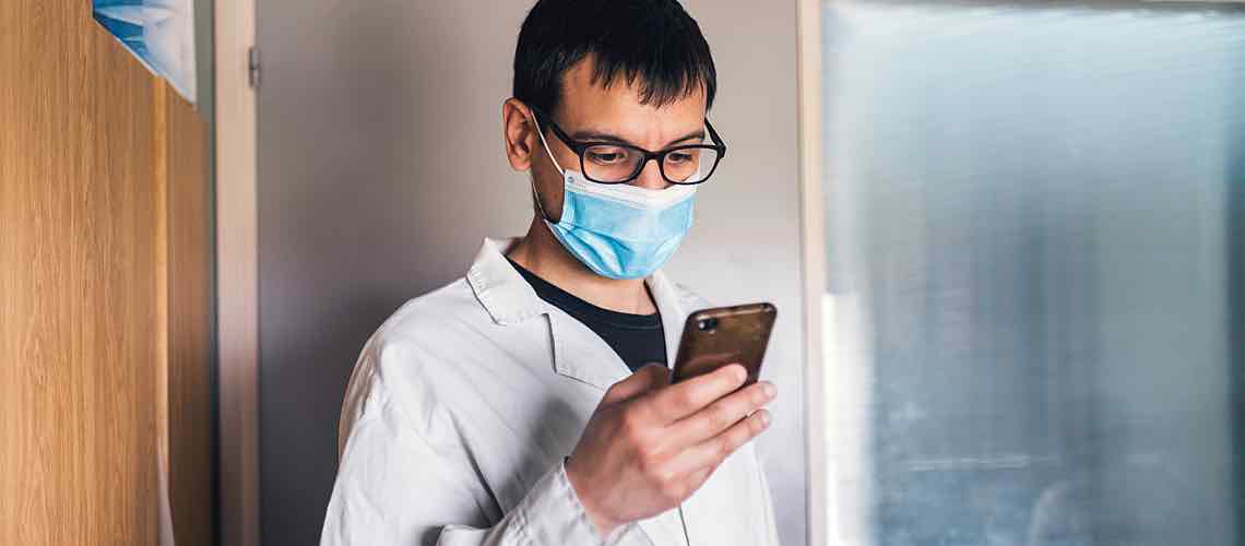 Scientist wearing mask looks at phone.