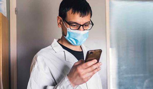 Scientist wearing mask looks at phone.