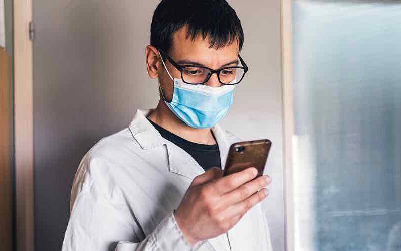 Scientist wearing mask looks at phone.